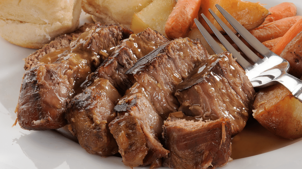 pedaços da carne na panela de pressão, cozida e suculenta, com o tridente de um garfo aparecendo rodeada de legumes como cenouras e batatas