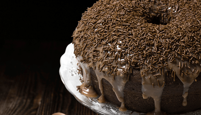 bolo de chocolate com furo no meio com cobertura de brigadeiro e chocolate granulado feito na airfryer servido em uma travessa de vidro que esta sobre a mesa madeira escura.