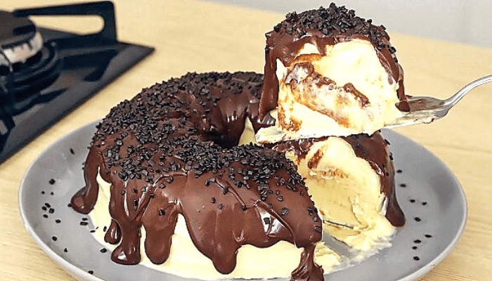 Pudim de sorvete servido em uma bandeja de cerâmica branca com cobertura de chocolate e um pedaço sendo retirado por uma colher de sobremesa