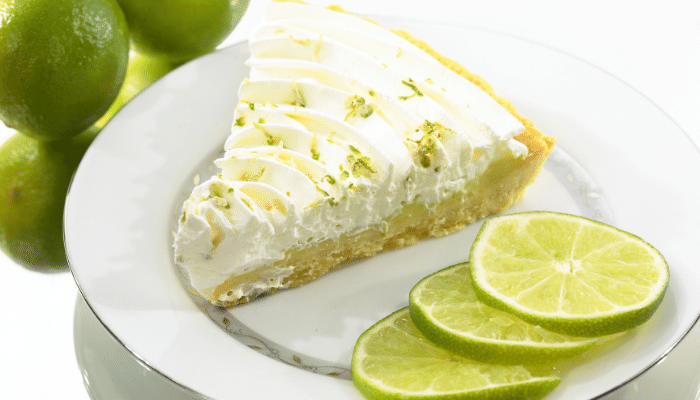 pedaço da torta de limão com merengue servido em um prato de cerâmica branco com 3 rodelas de limão usados para decoração