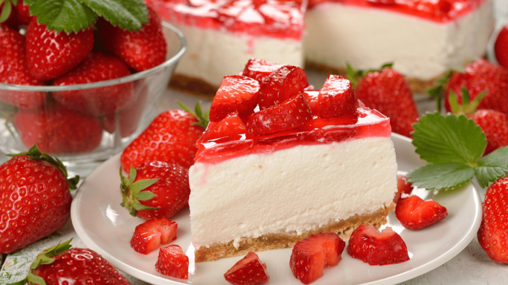 Um pedaço de Torta de morango servido em um prato de cerâmica branco com muitas frutas de morangos ao redor em forma de decoração do prato